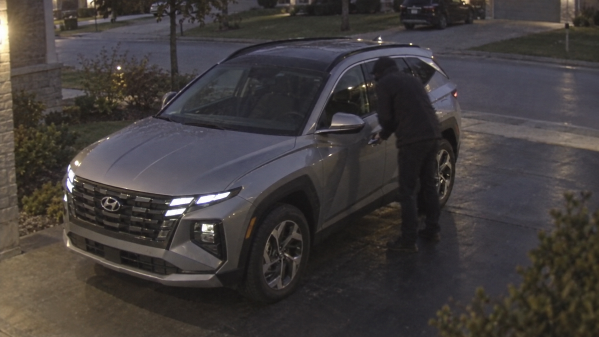 CCTV-style image of a Hyundai Tucson with a person attempting to open the driver’s door in a Canadian driveway at dusk.