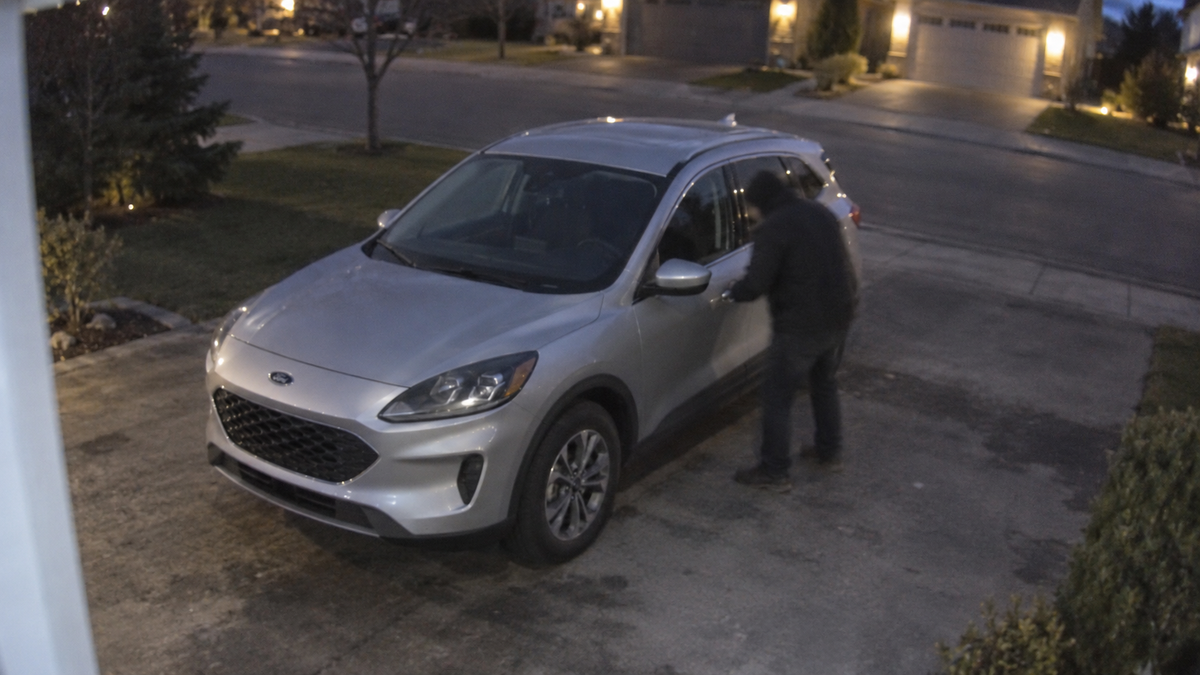 CCTV-style image of a silver Ford Escape with a person attempting to open the driver’s door in a Canadian driveway at dusk.
